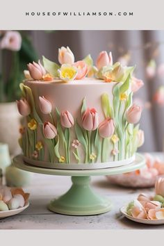 there is a cake decorated with tulips and flowers on the table next to plates