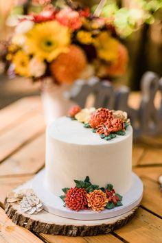 a white cake with flowers on it sitting on top of a wooden table next to a vase