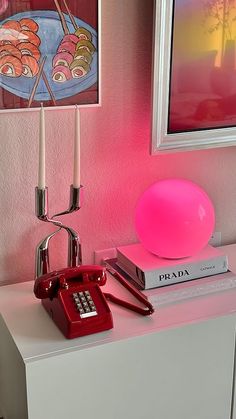 a table with a lamp, phone and books on it next to a pink wall