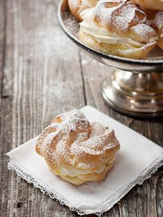 powdered sugar covered pastries sit on a napkin next to a silver plate with other pastries in the background