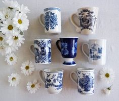 several blue and white coffee mugs with daisies on the table next to them