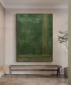 a large green painting hangs on the wall above a bench in a room with white walls