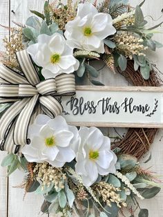 a wreath with white flowers and greenery on it that says, bess this home