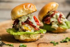 two mini sandwiches with lettuce and tomatoes on them sitting on a cutting board