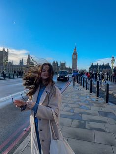 a woman is walking down the street with her hair blowing in the wind while wearing a trench coat