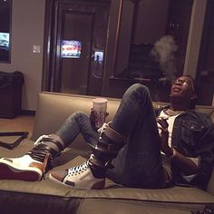 a man sitting on top of a couch next to a tv and holding a cup