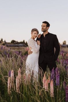 a man and woman standing next to each other in a field full of purple flowers