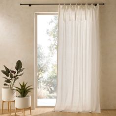 a white curtain hanging from a window next to two potted plants