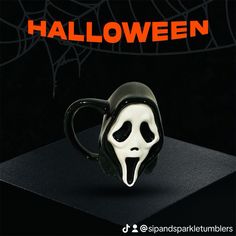 a black coffee mug with a ghost face on it and the words halloween written in orange