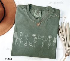 a t - shirt with scissors and flowers drawn on it next to a straw hat