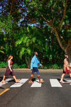 three people crossing the street in front of some trees