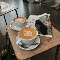 two cups of cappuccino sit on a table next to an open magazine