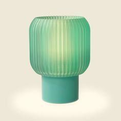 a green glass vase sitting on top of a table next to a white wall and floor