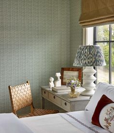 a bedroom with green wallpaper and white bedding has a chair next to the window