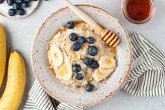 a bowl of oatmeal with blueberries, bananas and honey on the side