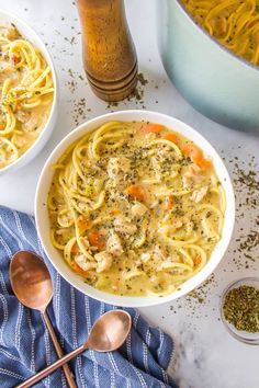 two bowls of chicken noodle soup on a table with silver spoons and a blue towel