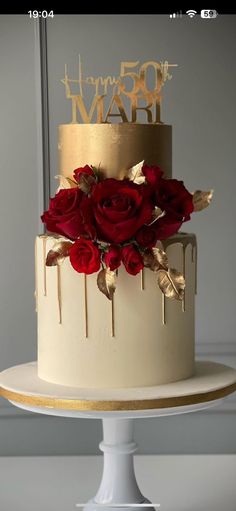 a white and gold wedding cake with red roses on the top tier is decorated with gold leaves