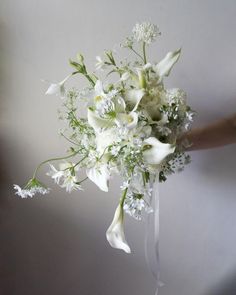 a bridal bouquet with white flowers and greenery is held by a woman's hand