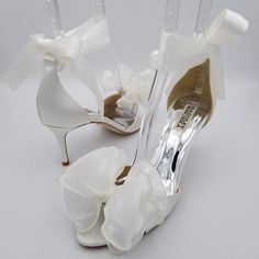 a pair of white high heel shoes with flowers on the toes and bows at the toe