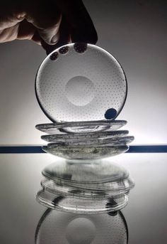 a stack of glass plates sitting on top of a reflective surface next to a person's hand