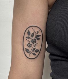 a woman's arm with a tattoo on it that has flowers and leaves in an oval frame