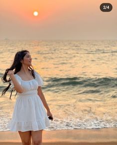 a woman walking on the beach at sunset with her long hair blowing in the wind