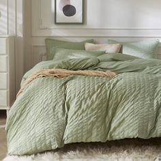 a bed with green comforter and pillows in a room next to a white dresser