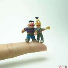 two small figurines sitting on top of a persons finger in front of a white background