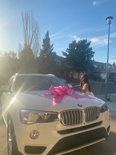 a woman standing next to a white car with a pink bow on it