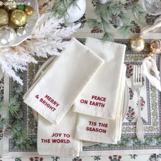 three white napkins with red words on them sitting next to silverware and christmas decorations