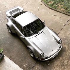 a silver sports car parked on top of a cement parking lot next to a green plant