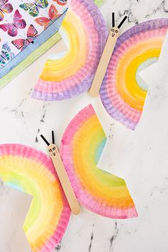 paper plate rainbows with clothes pins on them sitting on a marble table next to a book