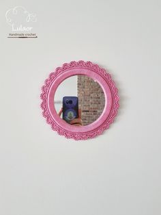 a person holding a camera in front of a pink mirror on a wall with the reflection of a brick building behind it