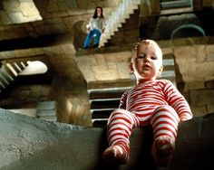 a small child sitting on top of a cement wall with stairs in the back ground