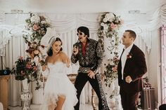 two men and a woman dressed up in wedding attire standing next to each other on stage