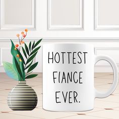 a white coffee mug with the words hottest fancy ever next to a potted plant