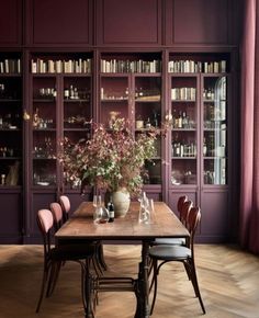 a dining room with purple walls and wooden table surrounded by bookshelves filled with wine bottles