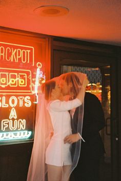 a man and woman kissing in front of a neon sign