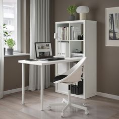 a white computer desk with a laptop on it in front of a bookcase and window