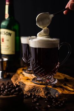 someone is spooning coffee into a cup with whipped cream on top and beans around it