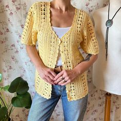 a woman standing next to a mannequin wearing a yellow crochet cardigan