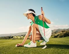 a woman kneeling on top of a green field holding a golf club