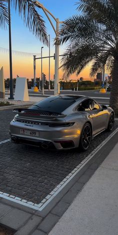 a silver sports car parked on the side of a road next to a palm tree