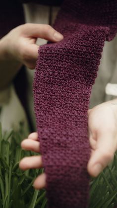 two hands holding a purple knitted neck tie in the middle of some green grass