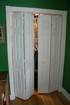 two white doors open in a room with green walls and hardwood floors, along with a wooden table