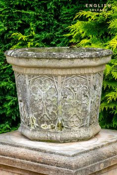 a stone planter sitting on top of a cement slab in front of some bushes