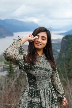 a woman in a green dress is holding her hand up to her eye and looking at the camera