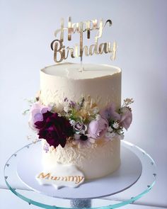 a birthday cake decorated with flowers and the words happy birthday written on top is sitting on a glass plate