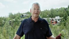 an older man is standing in front of some trees and houses with his hands out