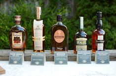 five bottles of different types of alcohol on a white tablecloth with trees in the background